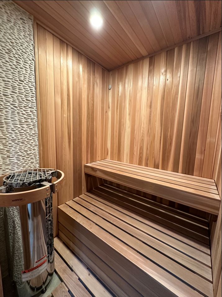 Cedar-lined sauna interior with pebble accent wall and Harvia heater